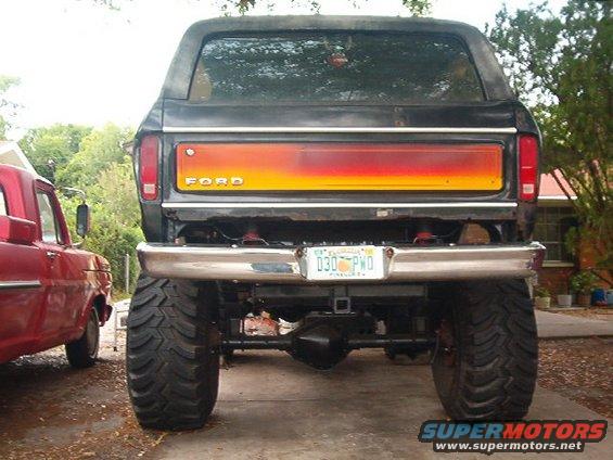 1979 Ford Bronco rear view, lifted with large tires and custom tailgate paint. Red truck parked to the left