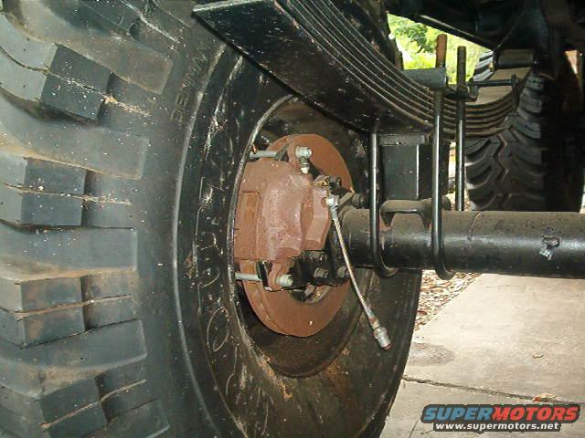 Close-up of a large, worn truck tire and rusty brake caliper with leaf springs visible