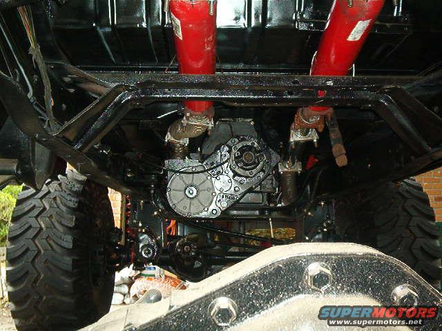 Underbody view of a vehicle with large tires, drivetrain, and red suspension components