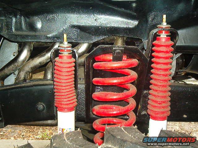 Close-up of red coil springs and shock absorbers mounted to vehicle frame