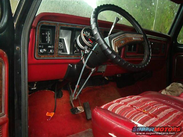 Interior shot of a vehicle with red seats and dashboard. Steering wheel and pedals are visible