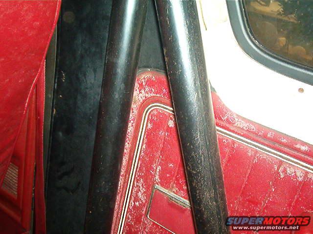 Interior view of a vehicle showing red quilted upholstery, black trim, and a black roll bar. A window is visible on the right