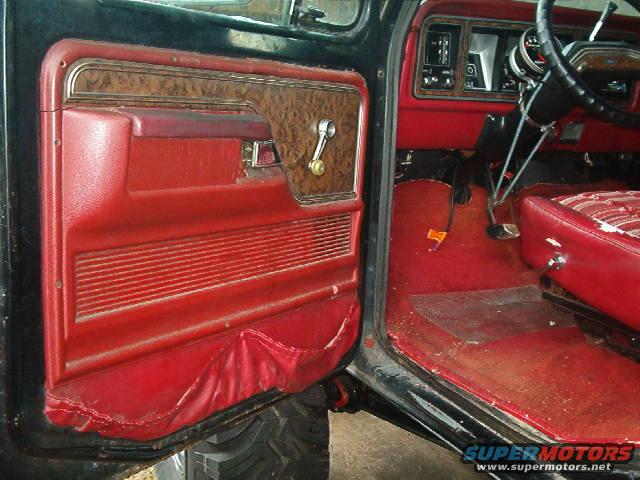 Red interior door panel with wood trim and chrome handle, dashboard, and seat