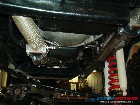 Underside view of a vehicle's exhaust and suspension system, showing a red coil spring and white shock absorber