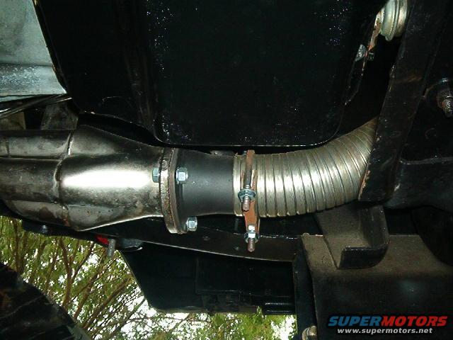 Exhaust pipe connection with flexible metal tubing and bolted flange. Black undercarriage visible