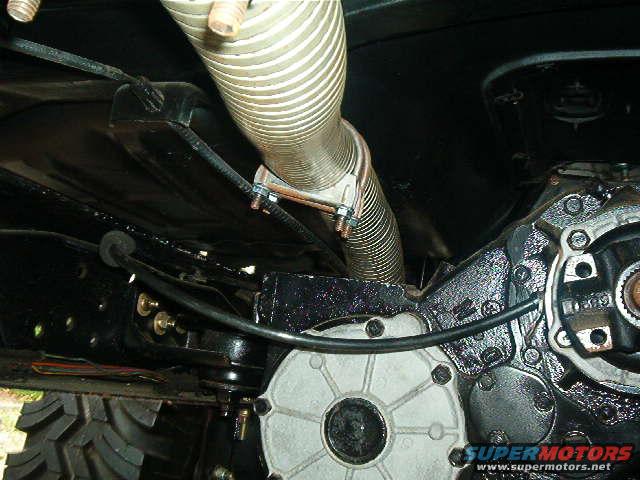 Underside of a vehicle showing exhaust pipe, transmission housing, and part of a tire