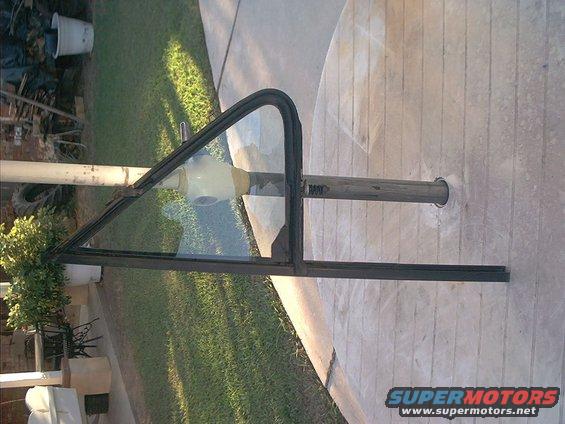 Vent window frame with black rubber trim and clear glass, attached to a metal pole