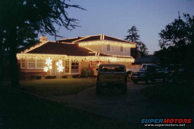 Yellow Toyota pickup truck and dark SUV parked in driveway of house with Christmas lights