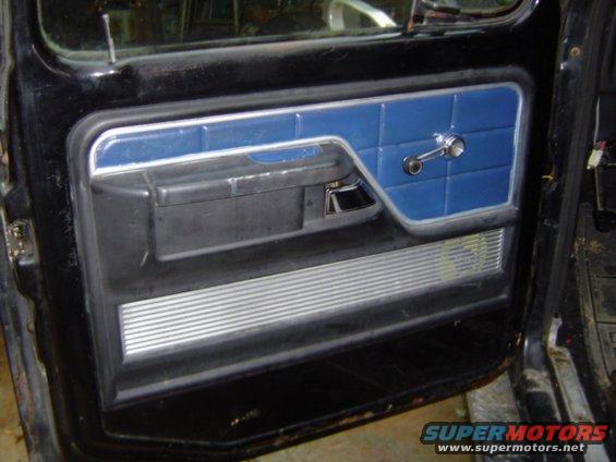 Close-up of a vehicle's interior door panel with blue upholstered sections and a chrome window crank