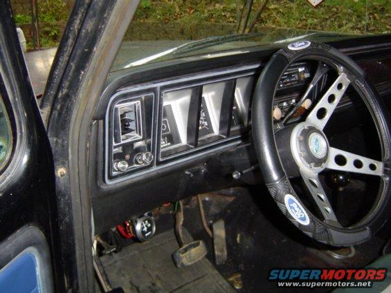 Dashboard and steering wheel of a 1979 Ford Bronco, showing a black dashboard with rectangular gauges and a silver steering wheel with a Ford logo