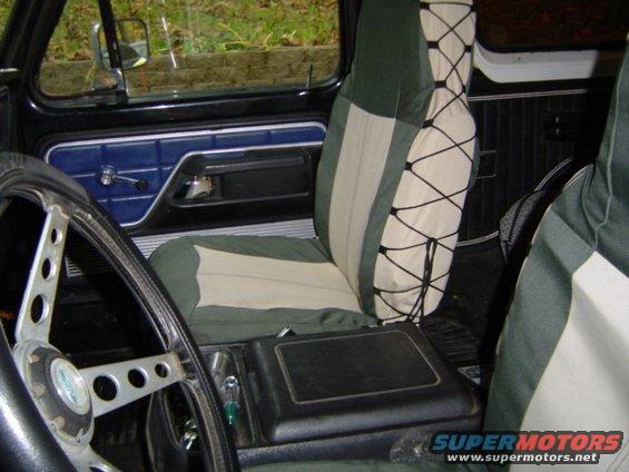 Interior view of vehicle with green and tan seat covers, aftermarket steering wheel, and center console