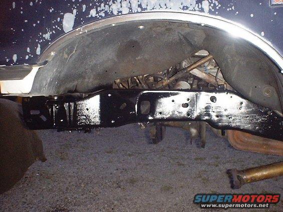 Black painted vehicle frame and suspension parts under wheel well. Exhaust pipe visible