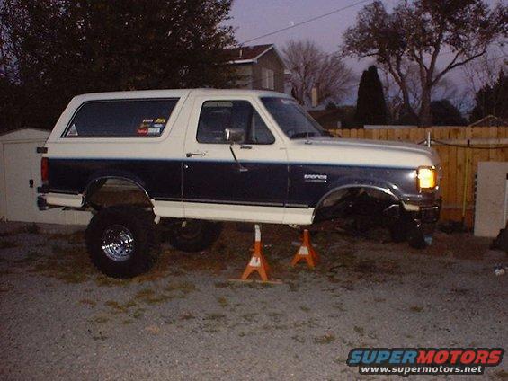 Two-tone Ford Bronco lifted on jack stands, front end partially disassembled