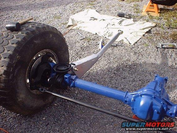 Front axle assembly with blue differential housing and large tire. A rubber mallet rests on the tire