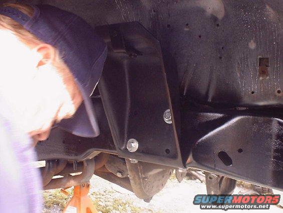 Close-up of a black metal bracket bolted to a vehicle's frame, with a person's head visible on the left