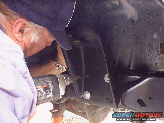 Man with drill working on vehicle frame, close-up on the action