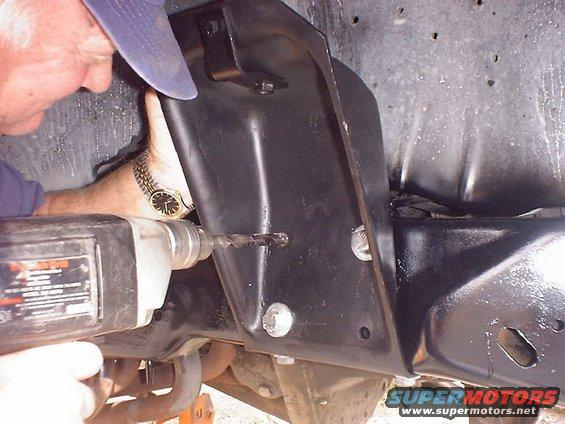 Drilling into black metal bracket on vehicle's front axle assembly