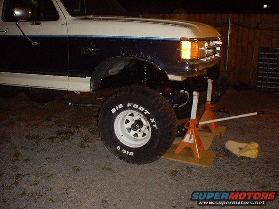 Front of a lifted Ford Bronco on jack stands, showing the front axle and a Big Foot XT tire