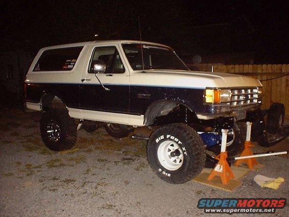 Two-tone blue and white Ford Bronco on jack stands, front axle removed