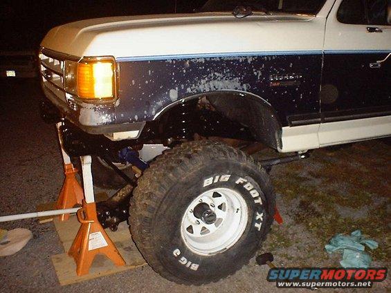 Front axle and Big Foot XT tire on a lifted truck, supported by jack stands
