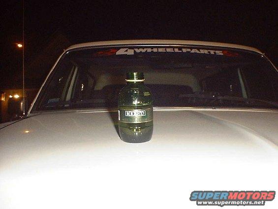 Green bottle on white car hood with '4 WHEELPARTS' sticker on windshield