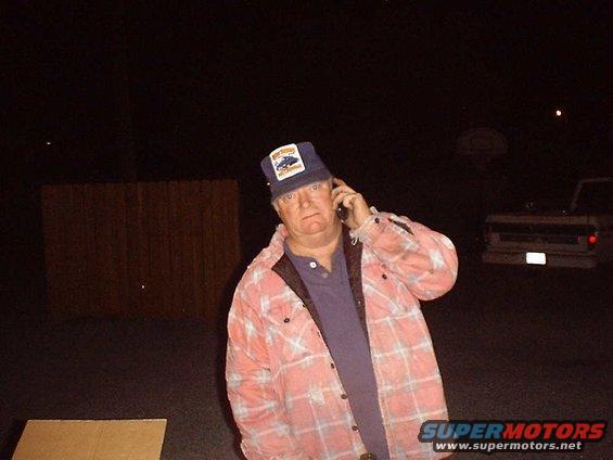 guy in plaid shirt and hat talking on cell phone, truck in background
