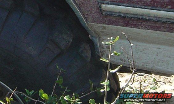 Underside of a dark tire and maroon body panel with a white trim strip