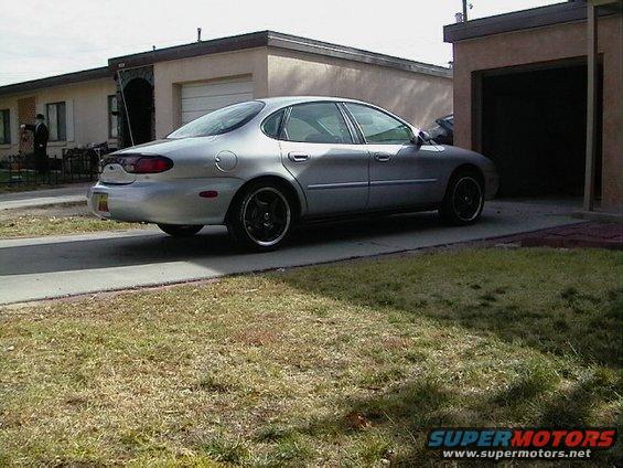 Silver sedan parked in driveway, side view. Black rims. House and garage in background