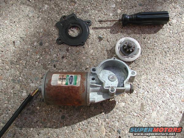 Ford power window motor disassembled with gears and screwdriver on concrete