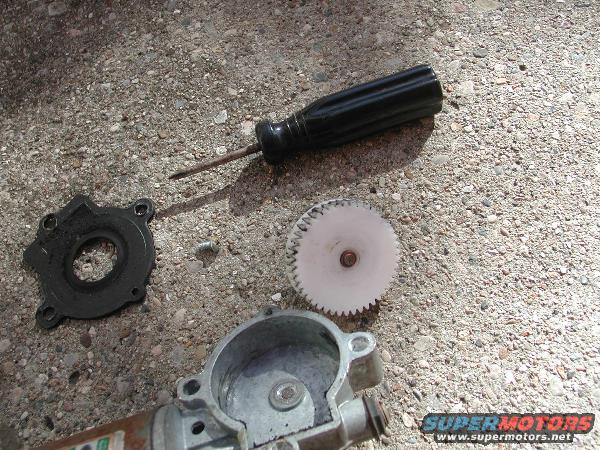 Car window motor parts including a gear, housing, and black plastic piece on concrete