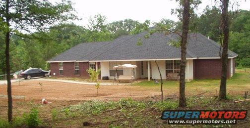 Dark sedan parked on a dirt driveway in front of a brick house