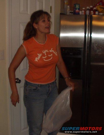 Woman in orange shirt and jeans holding a plastic bag