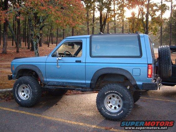 Blue 1986 Ford Bronco side view with off-road tires and spare tire on rear