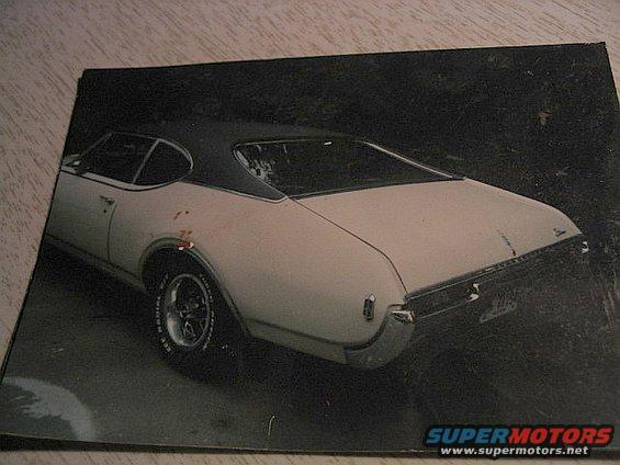 Rear 3/4 view of a white 1969 Oldsmobile 442 coupe with a black vinyl top