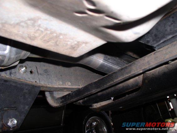 Underside view of a vehicle's exhaust pipe and frame, with a tire visible