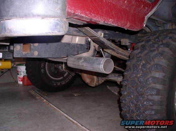 Underside of a vehicle showing exhaust pipe and large tire