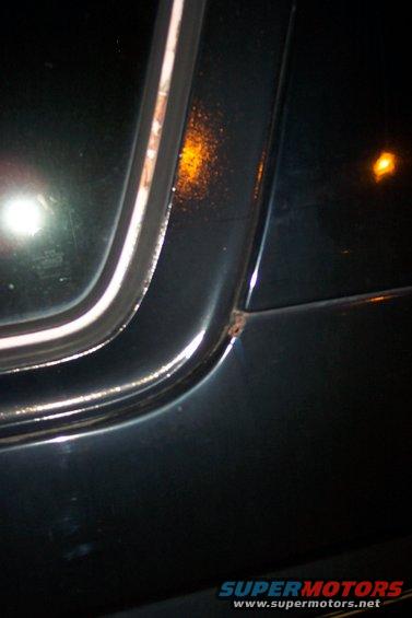 Dark vehicle body panel with window trim and rust spot
