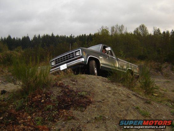 Dark green pickup truck driving up a dirt hill with trees in the background