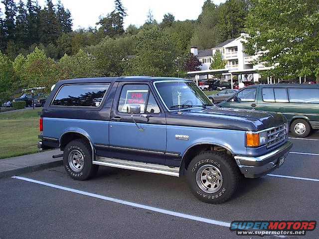 Blue and black 1988 Ford Bronco parked in a lot with a "For Sale" sign in the window