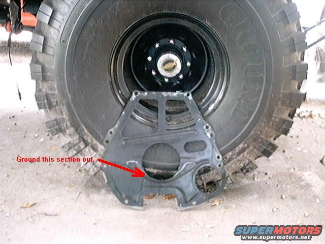 Engine plate in front of a large tire. Red arrow points to a section of the plate labeled 'Ground this section out.'