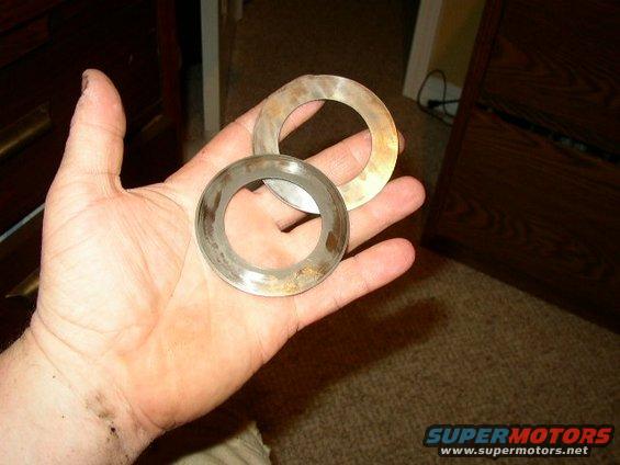 Two worn metal rings with brown discoloration held in a palm, with a wooden dresser in the background