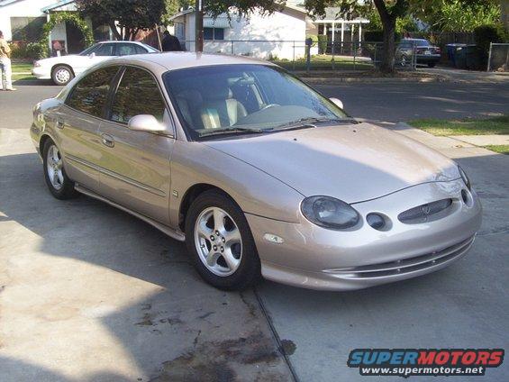 Tan sedan parked on a driveway, front quarter view. The car has tinted windows and alloy wheels