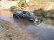 1988 Ford Bronco - This black SUV is partially submerged in a shallow creek, with water reaching its windowsills.