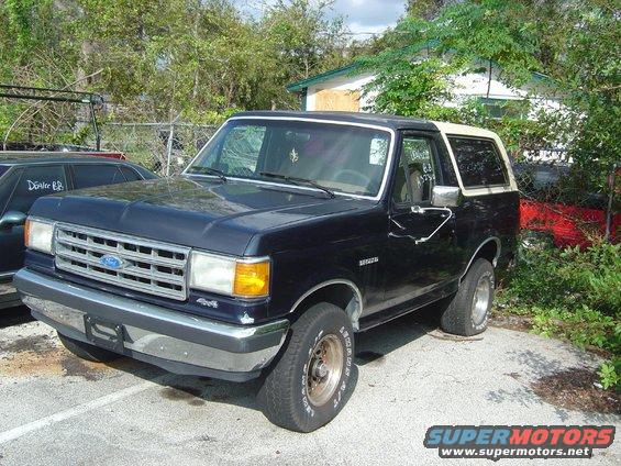 Dark blue Ford Bronco with a tan top, parked outside