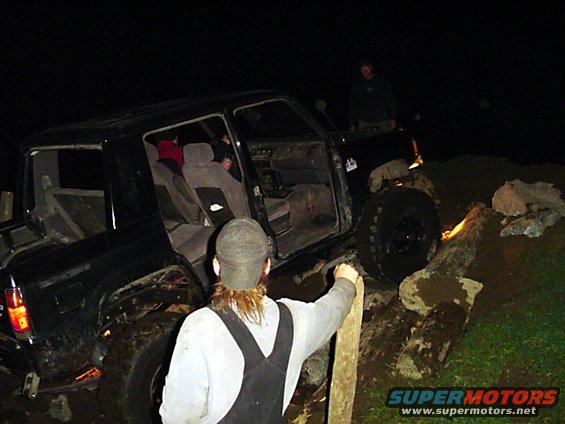 Black SUV with doors open, tires on logs, people around it at night