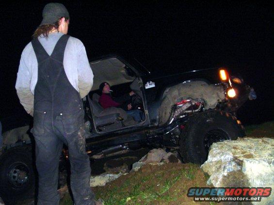 Black off-road SUV with large tires, lifted suspension, and people inside, angled from the front-right