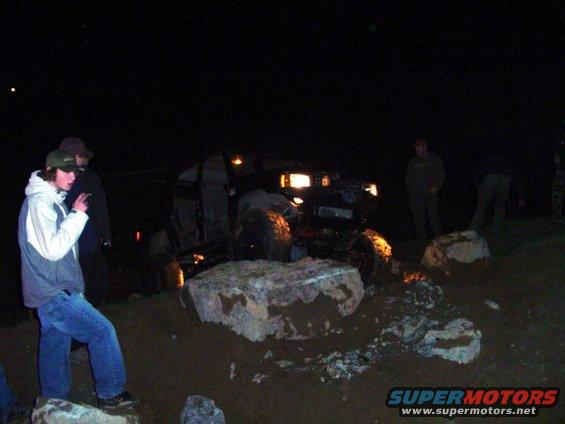 Off-road vehicle with headlights on, navigating rocky terrain at night