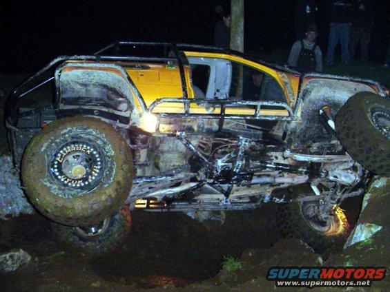 Yellow off-road SUV with roll cage and large tires tilted on rocky terrain at night