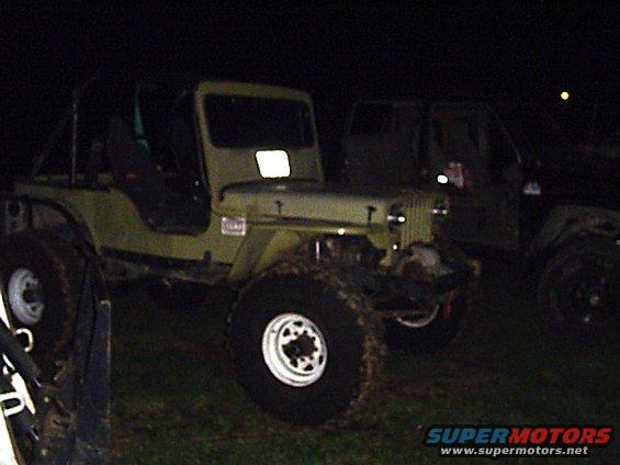 olive green Jeep CJ with large tires parked next to another vehicle at night