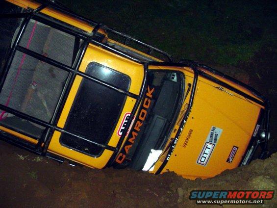 Yellow off-road vehicle with roll cage stuck in a ditch, has 'CAMROCK' and 'OTT STEERING AND GEARING' stickers